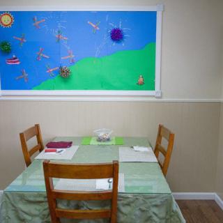 A small classroom setup with a table, chairs, and a decorated bulletin board on the wall.