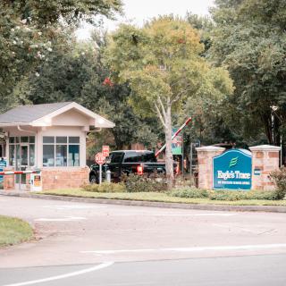 Entrance to a gated community with a security booth and a sign surrounded by trees.