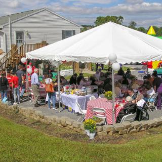 A lively outdoor community gathering under a large tent, featuring food and festivities.