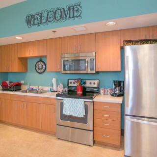 A modern kitchen with stainless steel appliances and wooden cabinets, featuring a welcome sign on blue walls.