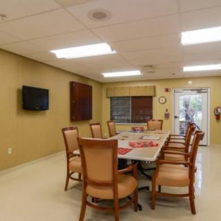 A well-lit conference room featuring a large meeting table surrounded by chairs, with a television mounted on the wall.