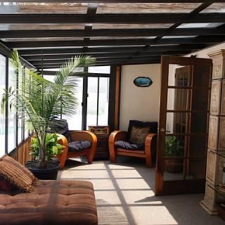 A cozy sunroom filled with natural light, featuring comfortable armchairs and lush indoor plants.