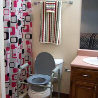 An accessible bathroom featuring a toilet with handrails and a colorful shower curtain.