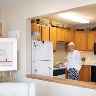 A woman standing in a kitchen of an apartment, with wooden cabinets and a refrigerator.