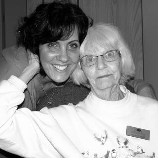 A black and white photo of two smiling women, one elderly and one younger, posing together indoors.