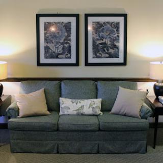 A cozy living room setup featuring a comfortable sofa adorned with decorative pillows and framed artwork on the walls.