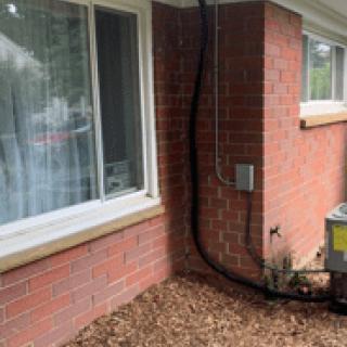 Outdoor view of a brick wall with large windows, an air conditioning unit, and pipes.