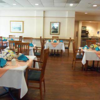 A neatly arranged dining area with tables set for service, featuring wooden chairs and a polished floor.