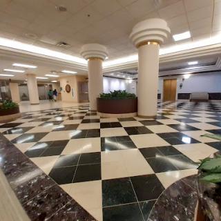 A spacious lobby featuring a checkered floor pattern with decorative columns and greenery.