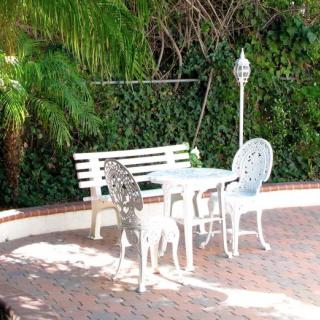 A cozy outdoor patio area with a white bench, table, and chairs surrounded by lush greenery.