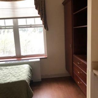 A simple bedroom with a bed, large window, and wooden wardrobe.