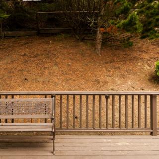 A wooden deck with a bench overlooking a yard surrounded by trees.