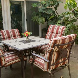 An outdoor patio set featuring a square table with cushioned chairs, surrounded by greenery.
