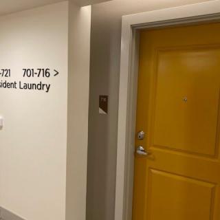 A hallway in a building with a yellow door and a sign indicating room numbers and student laundry.