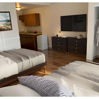 A modern hotel room with two beds, a television, a dresser, and a small kitchenette.
