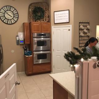 A cozy kitchen interior featuring a double oven, wall clock, and festive wreath.