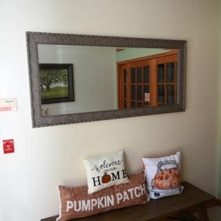A cozy interior space featuring a large mirror above a wooden bench adorned with decorative pillows, celebrating fall themes like 'Pumpkin Patch.'