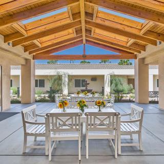 A sunlit outdoor patio with white dining furniture under wooden beams.