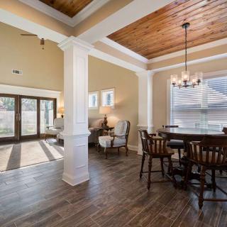 A well-lit dining room with a wooden floor and coffered ceiling, featuring elegant furniture and a chandelier.