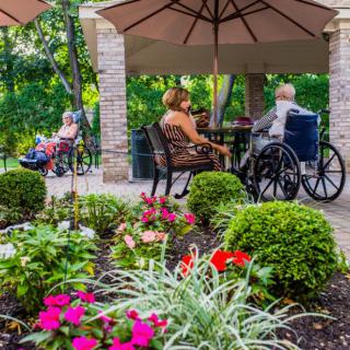 Seniors enjoy a peaceful afternoon in a garden patio setting, surrounded by colorful flowers.