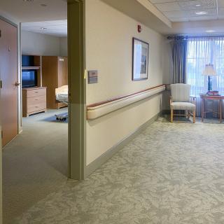 A hospital hallway leading to a patient room with furniture and medical equipment.