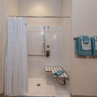A modern bathroom featuring an accessible shower with a folding seat and turquoise towels.