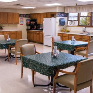 A cozy kitchen and dining area with tables, chairs, wooden cabinets, and a refrigerator.