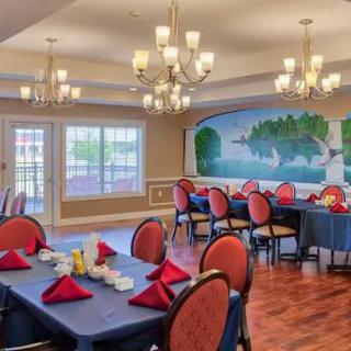 A well-decorated dining room with elegant chandeliers, mural on the wall, and tables set with red napkins.