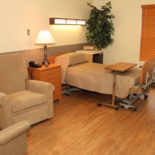 A well-furnished hospital room featuring a bed, chair, and bedside furniture.