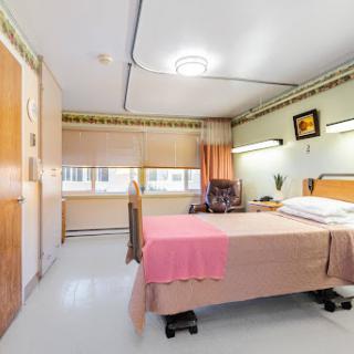 A clean and well-lit hospital room featuring a patient bed with a pink blanket, designed for comfort and care.