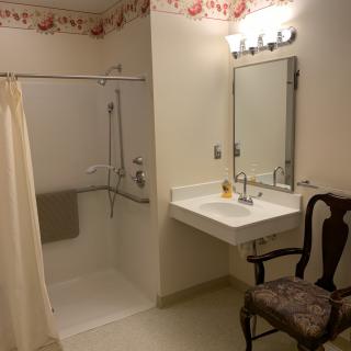 An accessible bathroom with a walk-in shower, sink, and chair.