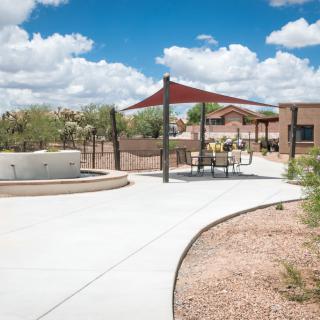 A sunny outdoor patio area with a shade structure and seating, surrounded by a desert landscape.