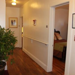 A well-lit hallway with wooden floors, a plant, and open doors leading to rooms.