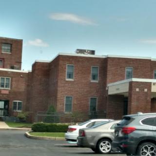 A brick building with a parking lot visible in front, set against a clear sky.
