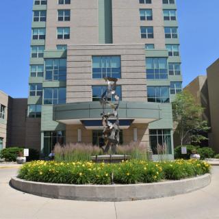 A modern building with a central sculpture and landscaped entrance.