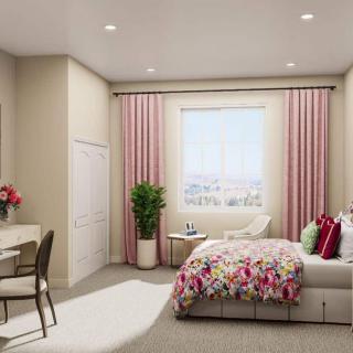 A cozy bedroom featuring a floral bedspread, pink curtains, and a small workspace.