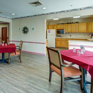 A cozy dining area with red tablecloths and a kitchen in the background.