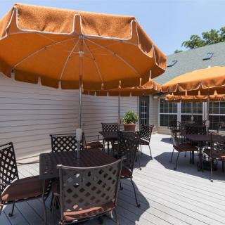 An outdoor patio with tables and chairs shaded by orange umbrellas on a sunny day.
