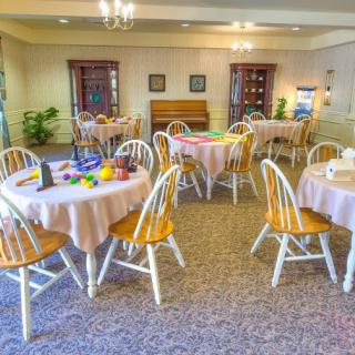 A well-lit dining room with round tables and wooden chairs set for a meal.