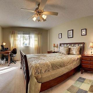 A cozy bedroom featuring a large bed, desk, and ceiling fan.