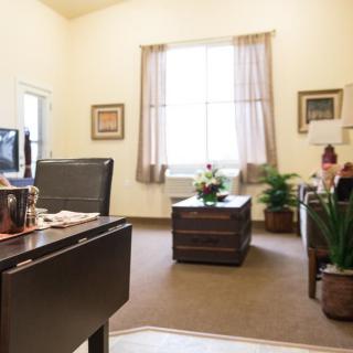 A cozy office space with a desk, chairs, and plants near a large window.