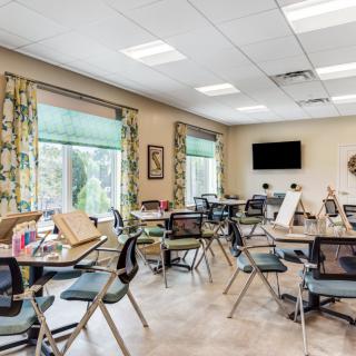 A well-lit classroom with tables and chairs, showcasing art supplies and a television on the wall.