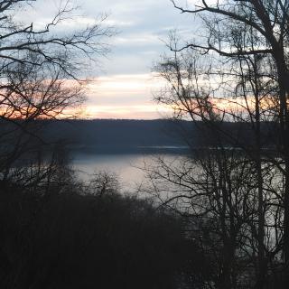 A tranquil view of a lake at sunset, framed by silhouetted trees.