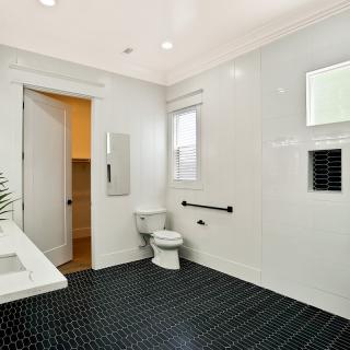 A modern bathroom with sleek white walls and dark floor tiles, featuring a toilet, sink, and mirror.