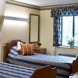 A cozy bedroom with twin beds, featuring a window with floral curtains and simple decor.