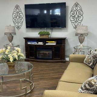 A cozy living room featuring a large sofa, a mounted television, decorative lamps, and a glass coffee table with flowers.