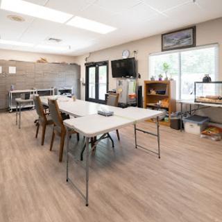 A spacious meeting room set up with tables and chairs, featuring ample natural light.