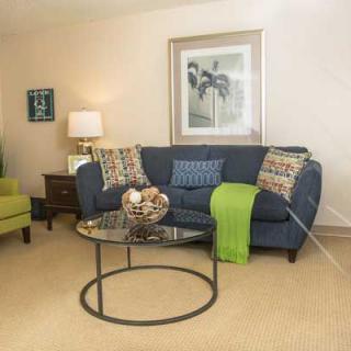 A cozy living room featuring a blue sofa with decorative pillows, a glass coffee table, an armchair, and artwork on the wall.
