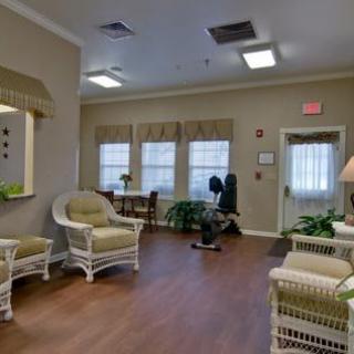 A cozy living room with wicker furniture and plants, featuring large windows that bring in natural light.
