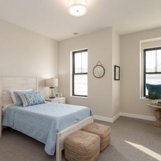 A modern and minimalist bedroom featuring a bed with blue linens, natural lighting, and neutral tones.
